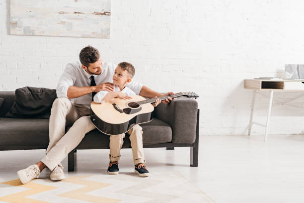dad teaching son to play acoustic guitar at home dad teaching son to play acoustic guitar at home father and son guitar stock pictures, royalty-free photos & images