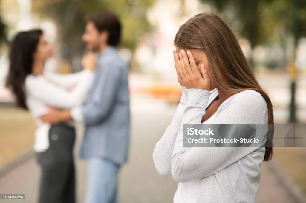 Upset woman crying, seeing her boyfriend with other girl Upset woman crying, seeing her boyfriend with other girl in park Infidelity Stock Photo