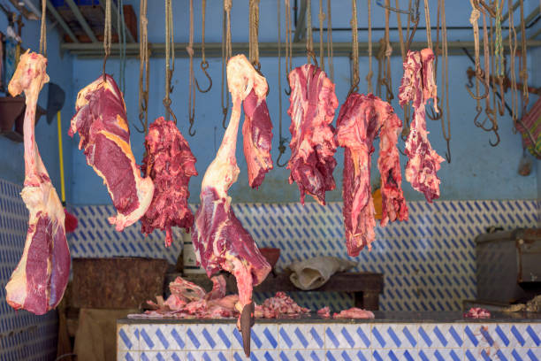 Fresh cuts of raw pork meat hanging on metal hooks at a traditional butcher stall in a wet market.