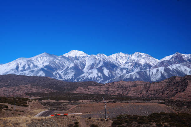 Landscape of Aconcagua national park, Mendoza, Argentina. In the foreground, a desert area with some short hills and a very few areas of vegetation. In the background, the Andes mountains covered with snow. Taken on a winter morning under a clear blue sky