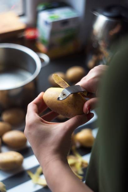 frau schälen kartoffeln über einem küchentisch - schälen essen zubereiten stock-fotos und bilder