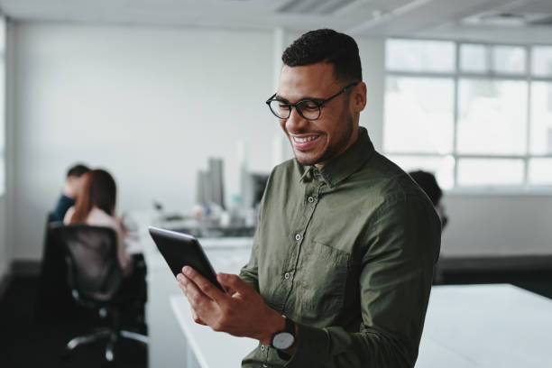 lächelnder junger geschäftsmann, der smartphone berührt und online-informationen im modernen büro überprüft - professional occupation business one person young adult stock-fotos und bilder