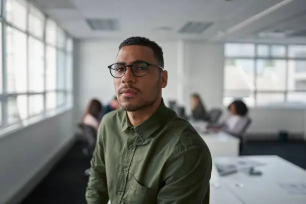 Photo of Portrait of a serious young professional businessman wearing eyeglasses looking at camera while colleague at background