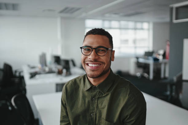 Friendly and smiling young african american professional businessman looking at camera in modern office Portrait of a positive young professional businessman in his office stubble male african ethnicity facial hair stock pictures, royalty-free photos & images