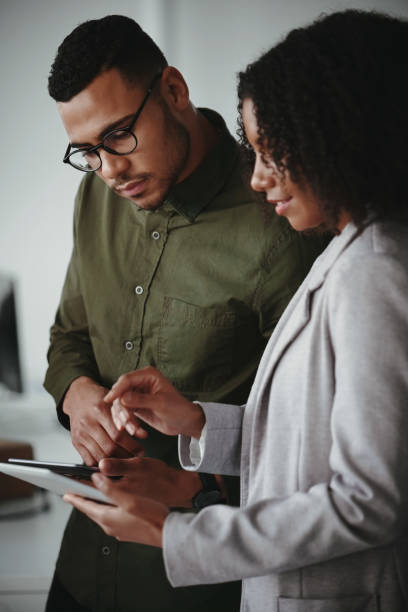 Young african american businessman and businesswoman discussing project on digital tablet computer in office Business partners discussing new ideas using digital tablet workplace diversity vertical stock pictures, royalty-free photos & images