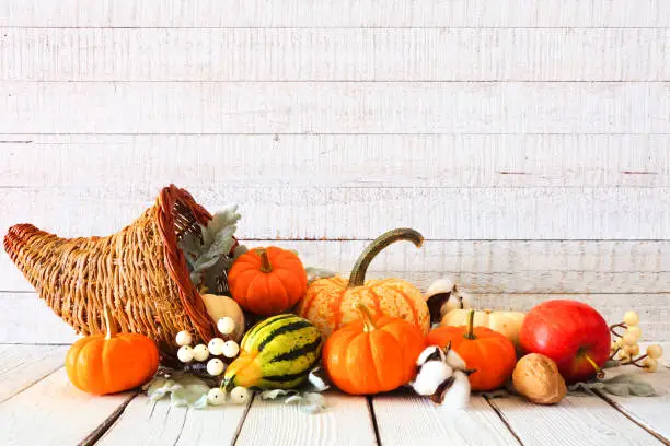 Photo of Thanksgiving cornucopia filled with autumn vegetables and pumpkins against white wood
