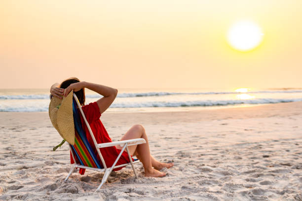 istock Model holding sun hat sitting on beach chair relaxing during sunset 1178154409