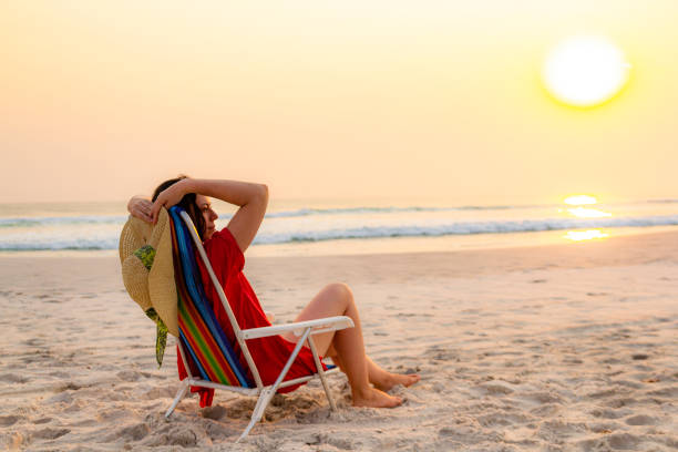 istock Model holding sun hat sitting on beach chair relaxing during sunset 1178154476