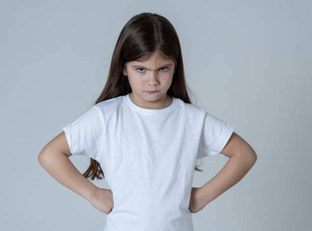Portrait of a cute pretty child girl looking angry and disappointed with her arms crossed. Isolated on neutral background. In children feelings and behaviour and human emotions and expressions. stock photo