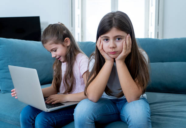 istock Sibling angry at younger sister spending too much time online using laptop. Digital technology addicted kid playing with computer ignoring her sad older sister. In children and internet addiction. 1178155115