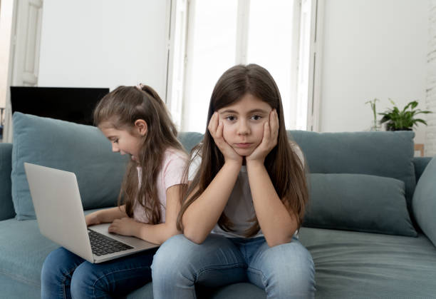 istock ibling angry at younger sister spending too much time online using laptop. Digital technology addicted kid playing with computer ignoring her sad older sister. In children and internet addiction. 1178155118