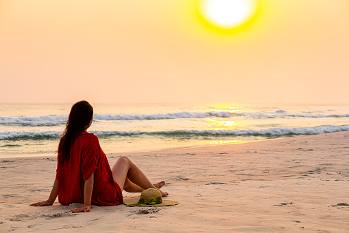 Woman sitting on sand with swimwear admiring sunset on the beach.