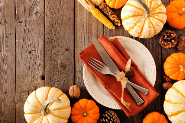 Autumn harvest or thanksgiving table setting with silverware, orange napkin, pumpkins and decor. Top view corner border against a rustic wood background.