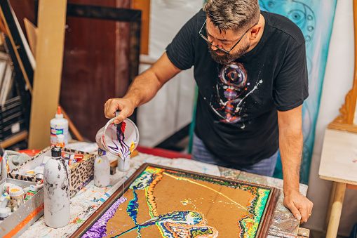 Male artist in his studio, pouring acrylic colors on canvas.