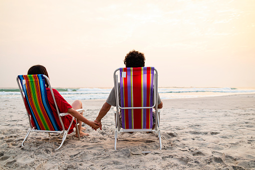 Couple holding hands on honeymoon at the beach. Beach concept at sunset.