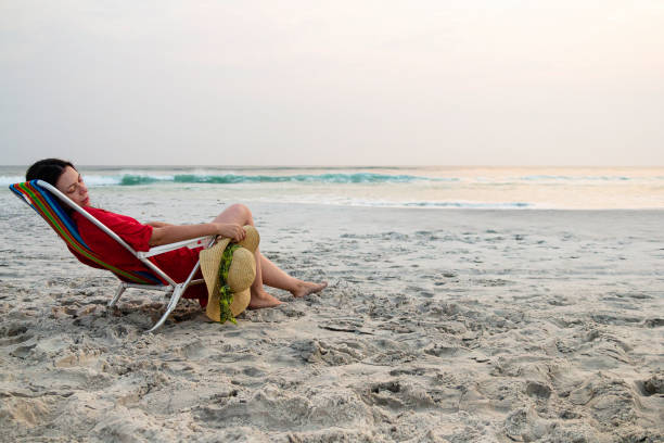 istock Model holding sun hat sitting on beach chair relaxing during sunset 1178162667