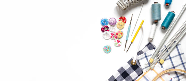 Sewing flat lay composition with threads, fabrics, scissors, buttons and sewing accessories on a white background, flat lay\nSet of sewing thread and accessories long banner