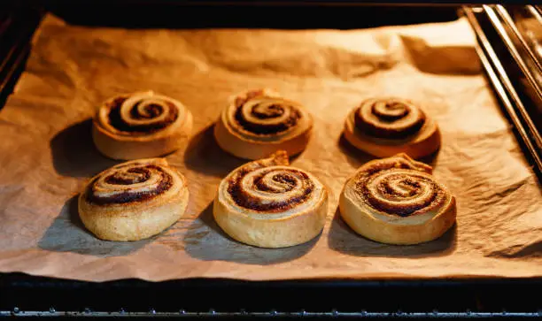 Sweet homemade vegan cinnamon rolls on baking paper in a lit up oven - Horizontal format