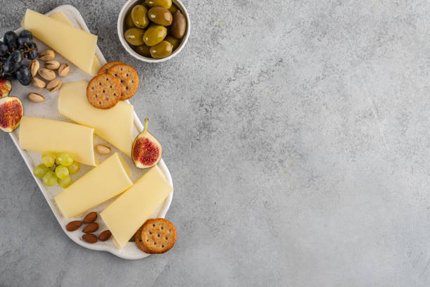 Cheese slices on white board with honey, figs, olives, grapes.