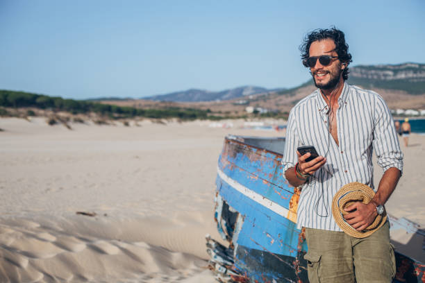istock Cheerful guy standing on the beach and using phone 1178167510