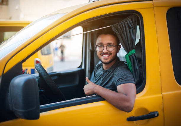 The taxi driver smiles happily, sitting in the cab of a yellow car stock photo