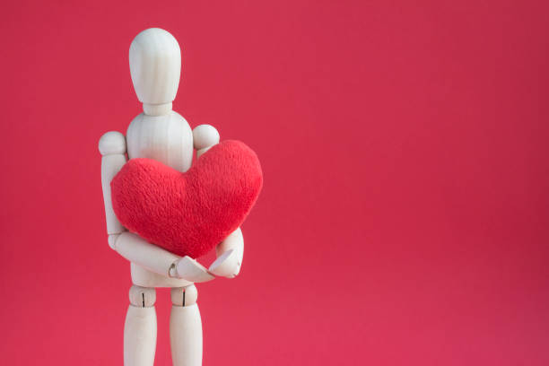 istock Wooden puppet human on red background holding red plush heart 1178172758