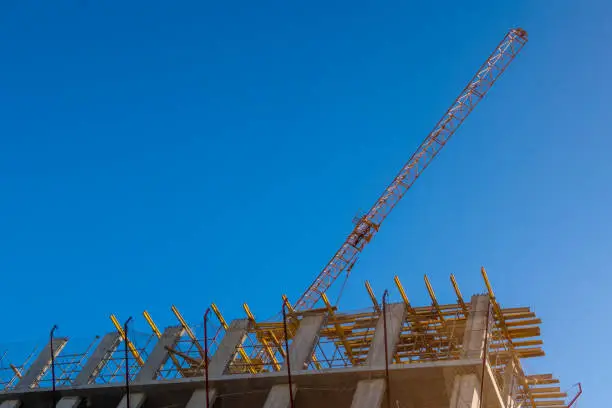 Building construction and arm of yellow crane against blue sky"n