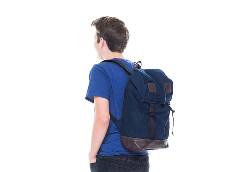 One man only / one person / rear view / waist up of 16-17 years old handsome people caucasian male / young men boys / teenage boys / student / high school student in front of white background wearing t-shirt / shirt / jeans / backpack with hands in pockets and holding bag / back to school