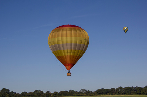 A golden hot air balloon flying above a treeline on a clear summer day