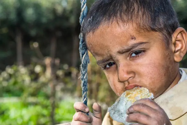 closeup of a poor staring hungry orphan boy in a refugee camp with sad expression on his face and his face and clothes are dirty and his eyes are full of pain