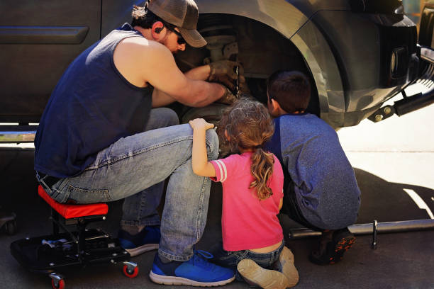 A young boy, a young auto worker, makes a tire change with a pneumatic wrench in the garage of a service station. A child learns the mechanics changing profession in auto repair service.