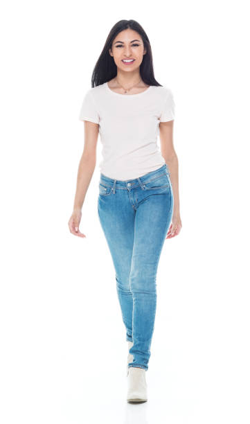 Front view / full length / one person of 20-29 years old adult beautiful / long hair latin american and hispanic ethnicity female / young women walking in front of white background wearing t-shirt / shirt / jeans who is smiling / happy / cheerful / cool attitude with hand by side vista frontal / longitud completa / una persona de 20-29 años de edad adulto hermoso / pelo largo latinoamericano y etnia hispana mujer / mujeres jóvenes caminando delante de fondo blanco usando camiseta / camisa / jeans que sonríe / feliz / alegre