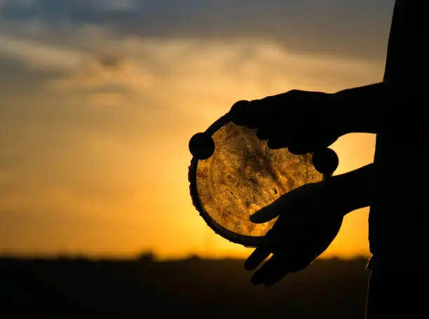 Hands holding a drum or tambourine performing a ritual healing ceremony on a background of the sky at sunset