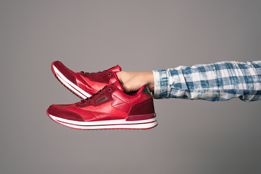Pair of new red sneakers in hand isolated on gray background.