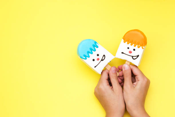 istock bright multicolored souffle dessert in white chocolate on a stick in hand with a smiley face on a yellow background dessert candies selective focus 1178206140