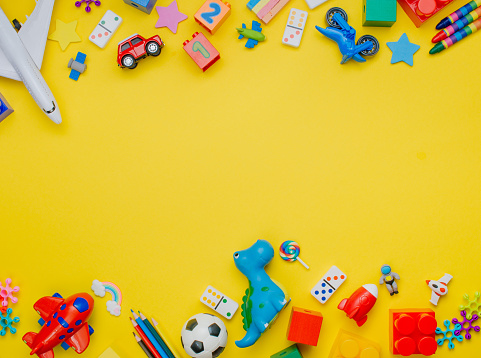Frame of kids toys on yellow background with blank space for text. Top view, flat lay.
