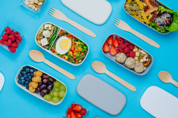 muster aus plastik-lunchboxen gefüllt mit gesunden lebensmitteln auf blauem hintergrund - bento box lunch healthy lifestyle stock-fotos und bilder