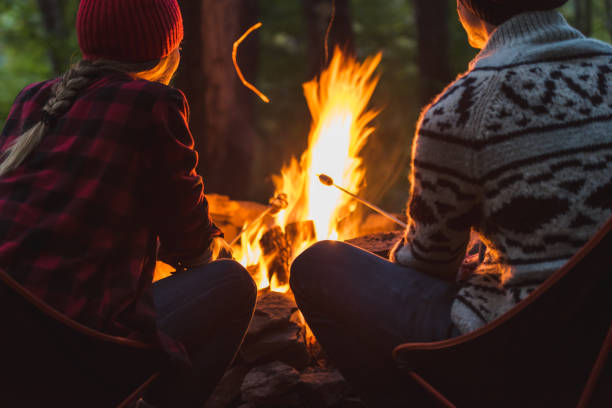A couple roast marshmallows together A young couple roasting marshmallows to make smores while camping. bonfire stock pictures, royalty-free photos & images