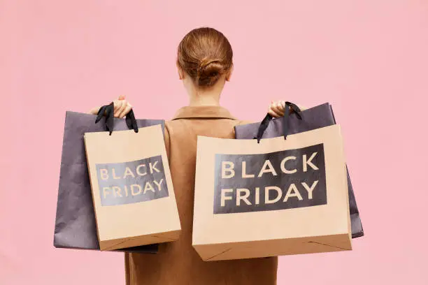 Photo of Rear view of unrecognizable woman with hair bun carrying black Friday paperbags on shoulders while leaving store