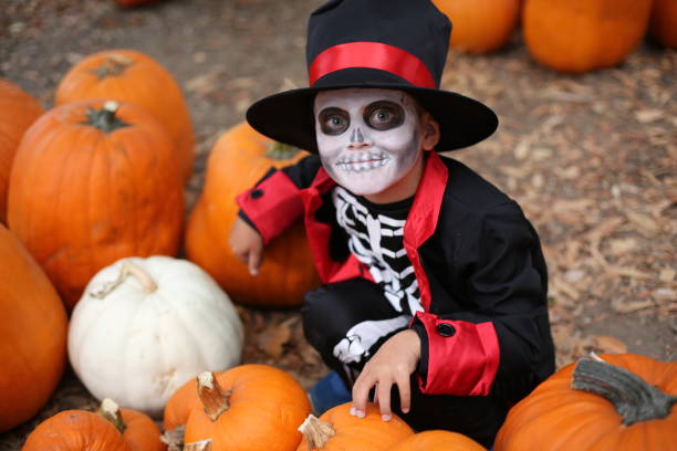 bambini di halloween che giocano a trick or treat. ragazzo in costume di halloween di scheletro con cappello e smock tra zucche arancioni. bambini di halloween - pumpkin child little girls pumpkin patch foto e immagini stock