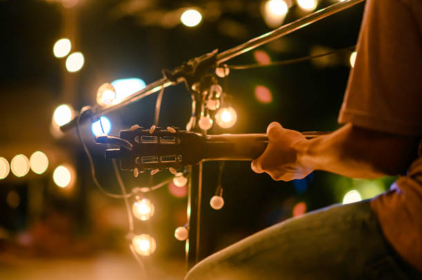 rear view of the man sitting play acoustic guitar on the outdoor concert with a microphone stand in the front, musical concept. - músico imagens e fotografias de stock