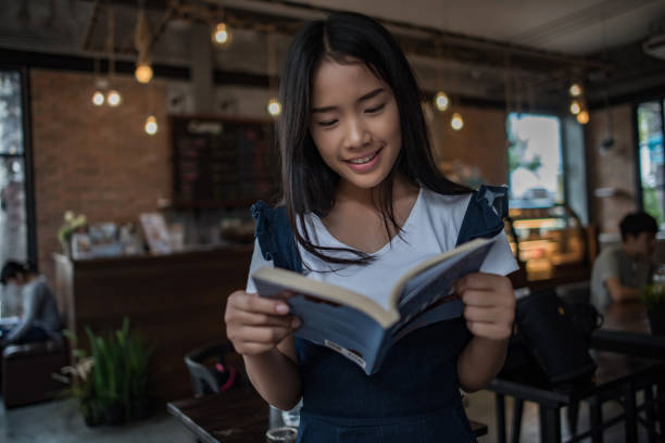 Young woman reading book sitting indoor in urban cafe.