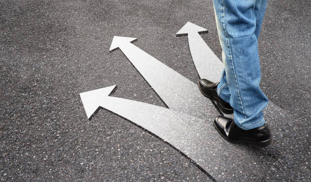 istock Business man standing on concrete floor with three arrows, left, right and front. Feet and white arrow sign on road. Different direction and success concept. Businessman walking in black leather shoes. 1178262275
