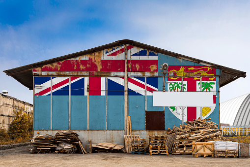 Close-up of the national flag of Fiji\n painted on the metal wall of a large warehouse the closed territory on a summer day. The concept of storage of goods, entry to a closed area, tourism