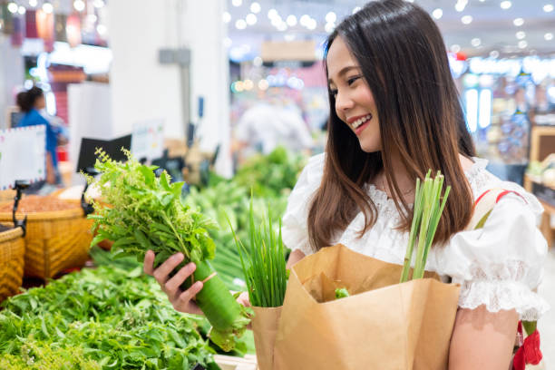 아시아 여성은 슈퍼마켓에서 야채를 구입합니다. 그녀는 종이 가방과 짠 가방을 사용합니다. 환경에 대 한 - tomato women green market 뉴스 사진 이미지