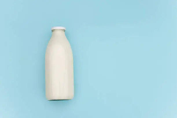 Milk in glass bottle on blue background with copy space. Flat lay Top view.