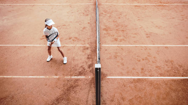 屋外クレーコートでテニスをしている子供。オープンテニスコートの小さなテニス選手のトップビュー。クラブでのテニストレーニングでスポーティな女の子のフルレングスショット。子供� - tennis court sports training tennis net ストックフォトと画像
