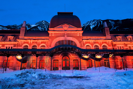 Old train station of Canfranc with the facade illuminated in reddish tones on a winter night with snow on the tracks,  Huesca, Aragón Spain