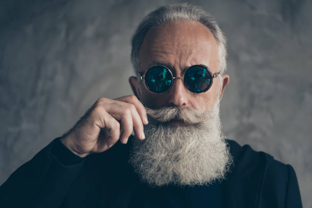 zbliżenie zdjęcie atrakcyjnego surowego męskiego emeryta w okularach okularowych dotykających jego wąsów odizolowanych na szarym tle - fashion rough jacket garment zdjęcia i obrazy z banku zdjęć