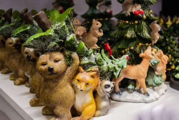 Photo of Christmas figurine: a squirrel sits on a Christmas tree carried by a bear, Fox, raccoon and a red cardinal bird on top. On a blurred background-the figure of a Christmas tree with an animals